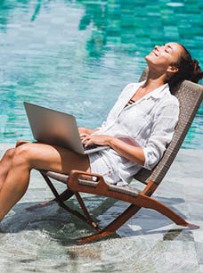 Woman working with laptop by the pool. Freelance work in tropical country